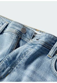 Vaaleansiniset farkut, joissa on metallinen napin suljin, vetoketjullinen etuläppä ja kontrastiväriset keltaiset tikit saumoissa.