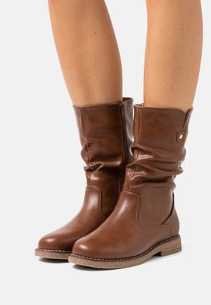 Bottes en cuir marron à la cheville avec un design décontracté, coutures contrastantes, fermeture éclair latérale et semelle en caoutchouc texturée.