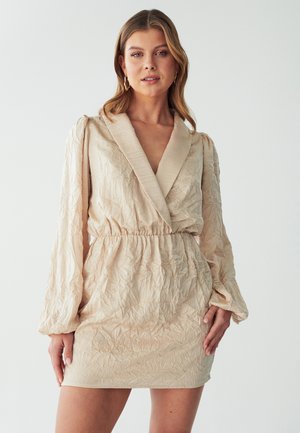 Beige mini dress with a textured, crumpled fabric, deep V-neck, wide collar, and elastic waistband. Long, billowy sleeves with gathered cuffs.