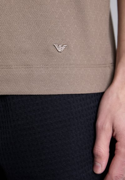 Kollane tekstuuriga topp väikese tikandiga logoga, millele on lisatud mustad tekstuuriga legginsid, näidates kangaste ja detailide lähedalt.