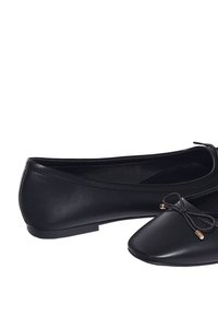 Ballerines en cuir noir avec un bout pointu, un design minimaliste et un petit nœud décoratif sur le devant. Semelle plate avec une texture lisse.