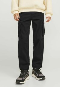 Black cargo pants made from durable fabric; features side pockets and a relaxed fit. Paired with black and gray sneakers.