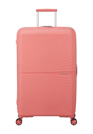 Grande valigia rigida color corallo con manico telescopico, quattro ruote girevoli, motivi a linee diagonali e orizzontali testurizzate e logo "American Tourister".