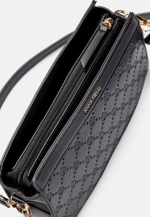 Bolso bandolera Anna Field de cuero negro con patrón circular en relieve, logo dorado, compartimento con cremallera y correa de cadena dorada desmontable.