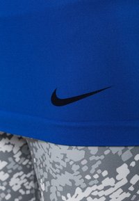 Sininen Nike urheilupaita, jossa on musta logo helmaosassa, yhdistettynä harmaisiin legginsseihin, joissa on teksturoitu kamouflagekuvio.