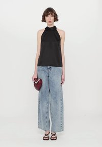 Melna satīna halter tops ar augstu kakla izgriezumu, kas apvienots ar gaiši ziliem platām biksēm. Modelis tur burgundijas krāsas rokassomu un valkā melnas sandales ar siksniņām.