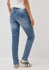 Blå denimjeans med smal passform, blekt mönster och bakfickor; tillsammans med grå och vita sneakers med gröna detaljer.