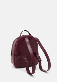 Ryggsäck i burgundyläder med rundad form, slät yta, två justerbara remmar och dragkedja upptill. Enkel design utan mönster.