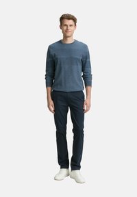 Dunkelblauer, strukturierter Pullover mit Rundhalsausschnitt, kombiniert mit schmal geschnittenen dunklen Hosen und weißen Sneakers. Der Pullover hat horizontale Streifen.