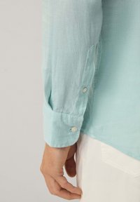 Licht turquoise linnen overhemd met lange mouwen, knopenmanchetten en een licht gestructureerde afwerking. Heeft een afgeronde zoom en subtiele stikdetails.