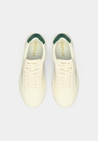 White sneakers with green accents, featuring a smooth synthetic upper, flat laces, and a cushioned insole with branded text inside.