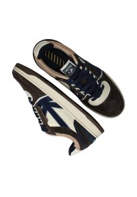 Baskets de sport en suède bleu marine et marron, avec des accents en cuir crème, une semelle blanche et des lacets bleus à motif texturé.