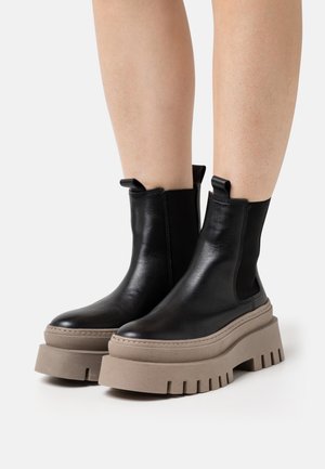 Czarne skórzane botki za kostkę z masywną beżową podeszwą na platformie, wyposażone w boczne elastyczne panele i pętelki ułatwiające zakładanie.