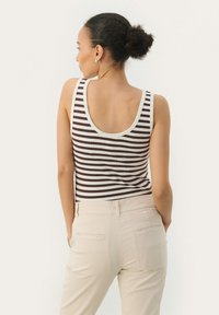 Brun og hvid stribet tanktop med scoop ryg, parret med beige bukser. Stoffet ser ribbet ud, med en tætsiddende silhuet.