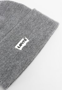 Gorro tejido gris con un puño doblado, que presenta un parche rectangular blanco con el logo de Levi's en la parte delantera. Textura suave con un diseño sencillo.