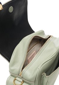 Groene leren handtas met een gestructureerde afwerking, gouden rits en een binnenzak met een label. Zwarte binnenkant met bovenste sluiting.