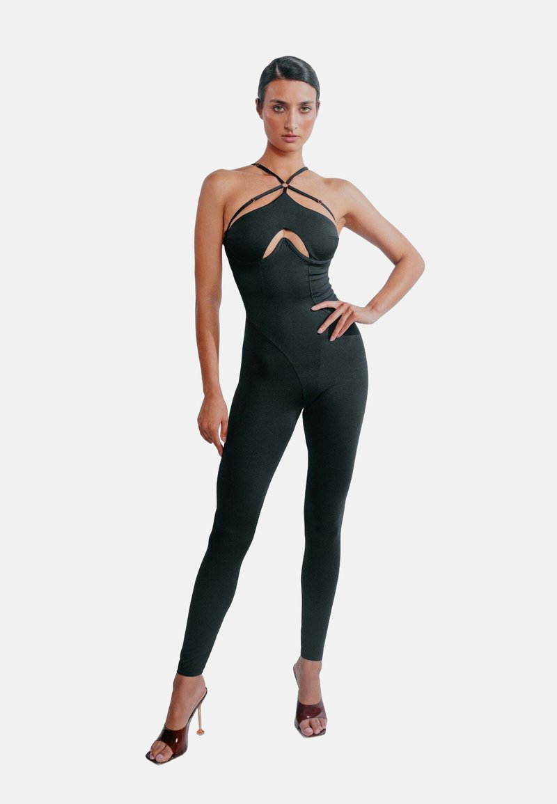 Svart byxdress med en åtsittande design, med en utskärning vid bröstet och korsade remmar. Slätt material, hel längd på benen, i kombination med högklackade skor.