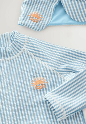Gestreifter blauer und weißer Rash Guard mit langen Ärmeln, bestickt mit einer orangefarbenen Sonne und Welle auf der Brust. Weicher Stoff.
