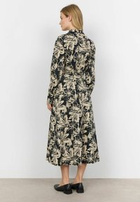 Zwarte midi-jurk met beige bloemenpatroon, lange mouwen, knoopsluiting, Getailleerde taille en uitlopende rok. G gedragen met zwarte instappers.