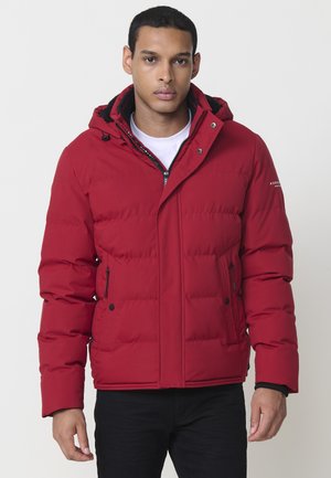 Chaqueta tipo puffer roja con capucha, que presenta un cierre con cremallera, dos bolsillos laterales y un diseño acolchado. Acentos negros alrededor del cuello.