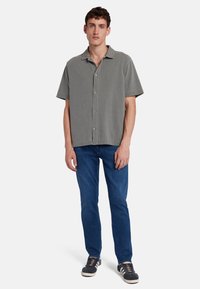 Camicia a maniche corte con colletto in tessuto verde tenue, con chiusura frontale a bottoni. Abbinata a jeans blu scuro e sneakers nere.