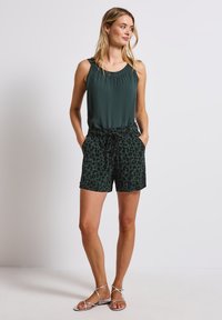 Tmavě zelený top bez rukávů se nařaseným výstřihem, spárovaný s černými šortkami s leopardím potiskem, které mají elastický pas a kapsy. Stříbrné sandály na pásky.