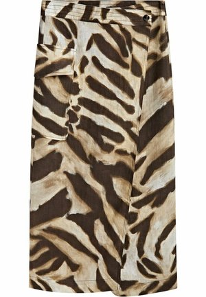 Personne à la peau foncée portant un haut à nouer blanc et un pantalon taille haute à rayures zèbre avec des poches, posant contre un mur clair.