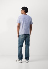 Tricou albastru cu dungi, cu guler rotund, asortat cu blugi din denim albastru deschis, cu buzunare și croială relaxată. Tenisi albi completează ținuta.