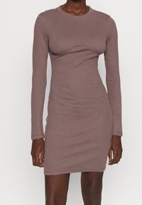 Langärmliges, geripptes Kleid in gedämpftem Mauve, mit figurbetontem Schnitt und einer geschwungenen Detaillinie über der Brust, aus einem dehnbaren Stoff gefertigt.