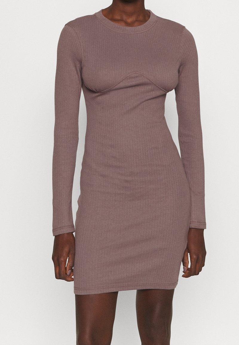 Langärmliges, geripptes Kleid in gedämpftem Mauve, mit figurbetontem Schnitt und einer geschwungenen Detaillinie über der Brust, aus einem dehnbaren Stoff gefertigt.