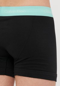 Schwarze Baumwollboxershorts mit einem hellblauen Calvin Klein-Logo-Bund und einer figurbetonten Passform. Verfügt über flache Nähte und eine moderate Länge.