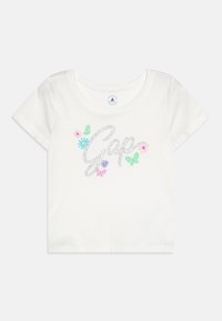 Hvid bomuld t-shirt med korte ærmer, der prydes af "Gap" i sølvglitter samt farverige blomster- og sommerfuglgrafikker. Rund halsudskæring.