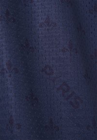 Tkanina námořnické modři s texturovanou, prodyšnou síťovinou a opakujícím se jemným vzorem fleur-de-lis. Vyznačuje se jemným tkaním a měkkým povrchem.