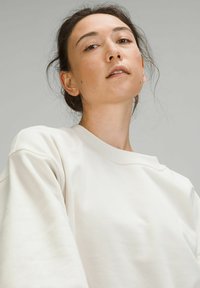 Licht beige sweatshirt met een losse pasvorm, een brede ronde hals en een textuurstof. De mouwen zijn licht gepoft bij de schouders.