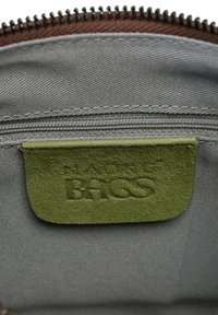 Hnedá vnútorná kapsa so zipsom s textúrovanou zelenou koženou štítkou s embosovaným nápisom „BAGS.“ Viditeľná hladká sivá podšívka.