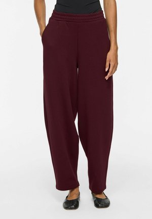 Pantalon ample bordeaux foncé avec taille élastique et poches, porté avec des ballerines noires et un haut noir, montré de la taille vers le bas.