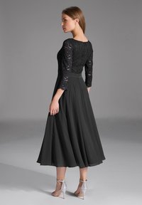 Robe de soirée noire avec un corsage en dentelle et des manches trois-quarts, jupe en satin évasée, et talons argentés avec lanières. Texture lisse, design élégant.