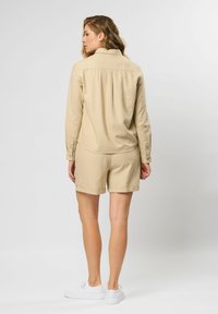 Beige langemouwen shirt gecombineerd met bijpassende korte broek, beide gemaakt van lichtgewicht stof. Witte sneakers maken de outfit compleet.