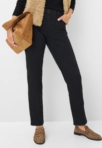 Pantalons noirs taille haute en coton, associés à un sac en daim beige. Des chaussures à imprimé animal à enfiler complètent le look.