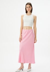 Top corto bianco a costine, gonna midi in raso rosa, texture liscia, orlo svasato, abbinato a ballerine bianche con punte a forma di fiocco.