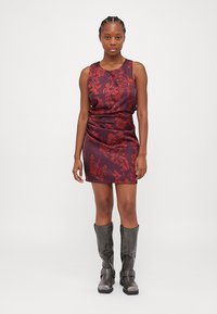 Maroon sleeveless dress with a floral pattern in red. Smooth fabric with a fitted bodice, ruched detail, and a straight skirt. Styled with gray knee-high boots.