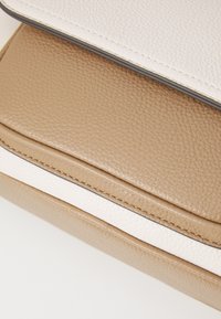 Lærveske med en teksturert beige bunn og en glatt hvit klaff, fremhevet av kontrastsøm og en elegant silhuett.