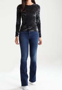 Svart sammet långärmad topp med blommönster, kombinerad med utsvängda blå jeans och vita skor. Enkelt och figursytt design.