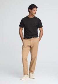 Svart bomullst-shirt med korta ärmar och en liten logotyp. Beige twillbyxor med raka ben, kombinerade med ljusa sneakers. Enkel design.