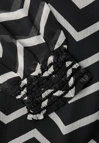 Černo-bíle žebrovaná látka se zřaseným elastickým manžetovým detailem.