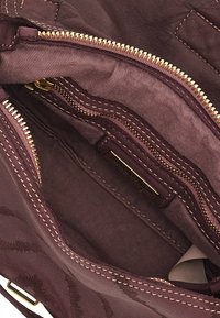 Interno di una borsa in pelle bordeaux scuro con numerosi zip dorati, texture di tessuto morbido e un'etichetta. Facce cucite lungo i bordi.