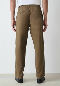 Khaki trousers with a smooth texture, featuring a straight cut, two back pockets, and a classic waistband design. Paired with black footwear.