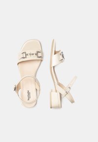 Sandali beige con finitura lucida, ampia fascia con dettagli in argento, cinturino regolabile alla caviglia e tacco basso a blocco.
