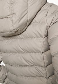 Lysegrå dunjakke med hætte, der har quiltede sektioner, glat tekstur og diskrete syningsdetaljer.