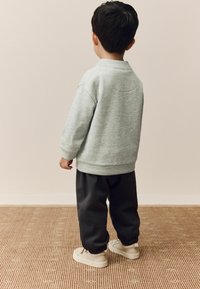 Grijze sweatshirt met een ontspannen pasvorm, donkere trainingsbroek en beige sneakers met elastische boorden. Zachte textuur en eenvoudig ontwerp.